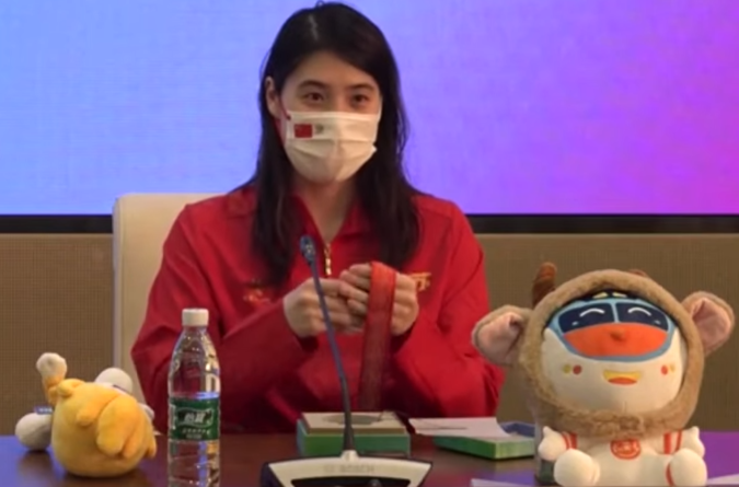 资料图：图中为张雨霏身穿红色运动服佩戴口罩出席发布会并手拿奖牌的场景。